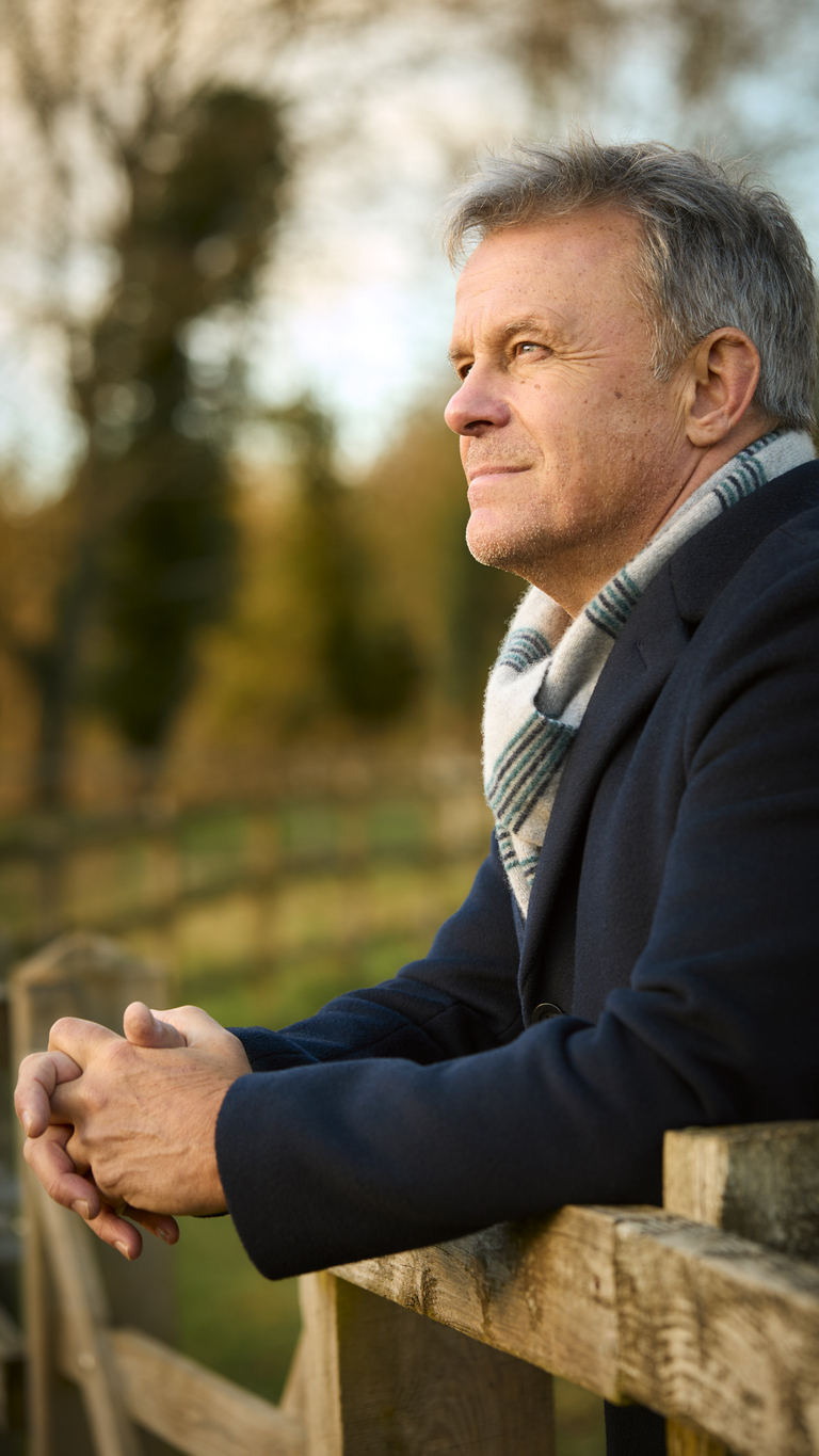 Smiling Senior Man Leaning On Wooden Fence On Walk Through Autumn Park Or Countryside
