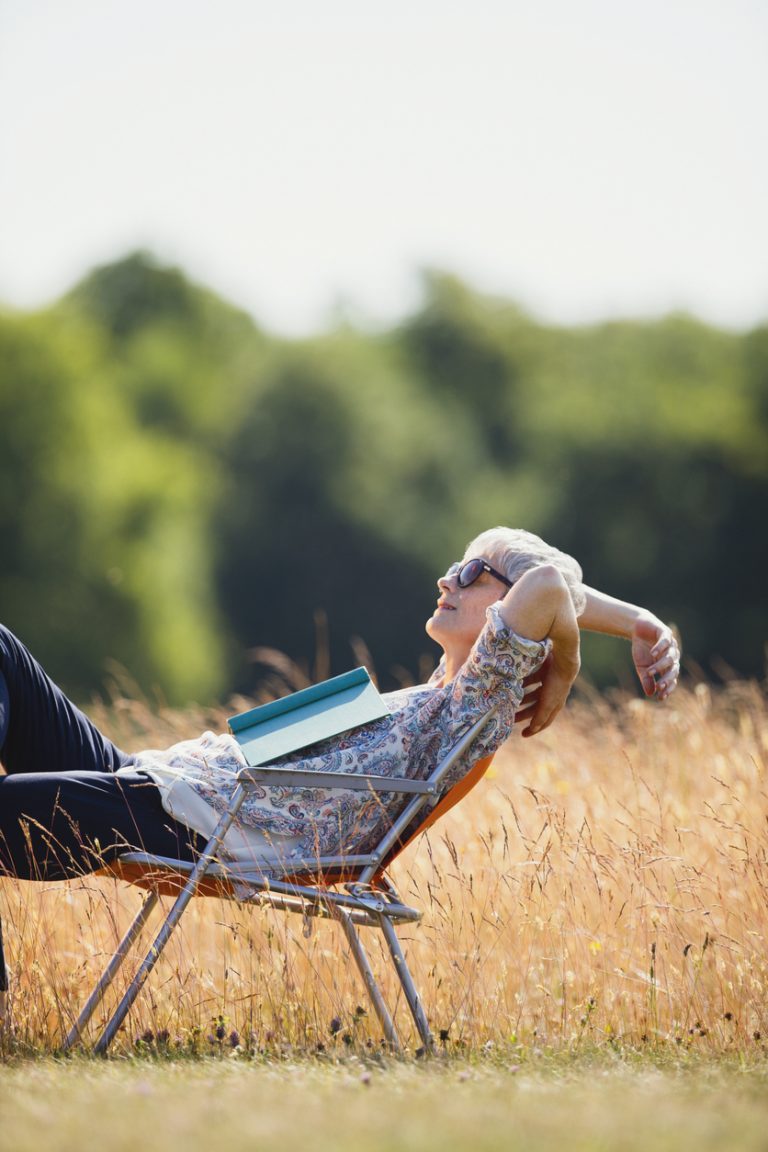 Carefree senior woman relaxing with book in sunny field